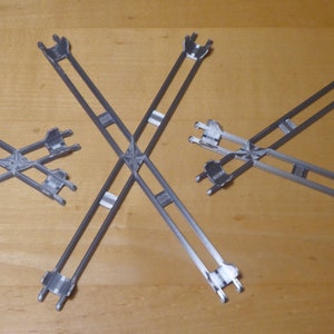 May include: Three silver metal frames in the shape of a cross. The frames are different sizes and are arranged in a row on a wooden surface.