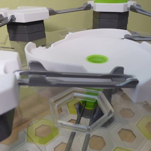 Puede incluir: Un circuito de canicas de plástico blanco con una pista gris y una base verde. La pista es curva y tiene un pequeño agujero en el centro. La base está hecha de un patrón de panal.