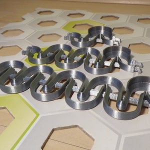 Puede incluir: Un conjunto de cinco organizadores de cables de plástico gris, cada uno con una serie de bucles entrelazados, diseñados para mantener los cables ordenados y organizados.