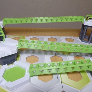 Könnte beinhalten: Eine grüne Plastikspielzeugbrücke mit einem dreieckigen Muster. Die Brücke ist mit einem weißen und grauen Spielzeugbauwerk mit einer Leiter verbunden.