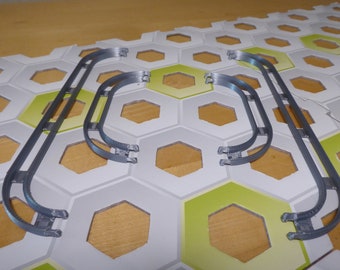 Pode incluir: Três peças de plástico cinzento que parecem corrimãos curvos. As peças estão sobre um fundo hexagonal branco e verde.
