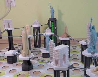 Puede incluir: Un juego de mesa con réplicas en miniatura de monumentos famosos, incluyendo la Torre Eiffel, la Estatua de la Libertad y la Torre Inclinada de Pisa. Las piezas del juego están conectadas por varillas metálicas y están dispuestas en un tablero de juego hexagonal.