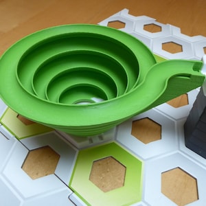 Könnte beinhalten: Eine grüne Spielzeugbahn aus Kunststoff mit einer spiralförmigen Rampe und einer weißen Kunststoffbasis. Die Bahn ist für Murmeln oder andere kleine Gegenstände zum Herunterrollen konzipiert.