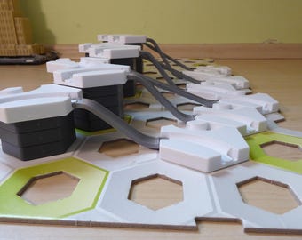 Puede incluir: Un juego de bloques de construcción modulares con componentes blancos y grises. El juego presenta placas base hexagonales con detalles en verde y amarillo, conectadas por tubos grises. Los bloques tienen un diseño futurista.