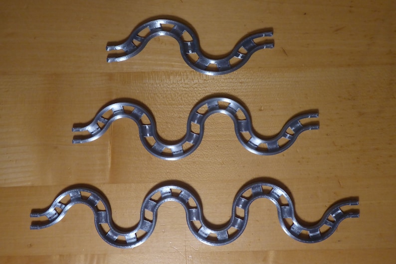 Puede incluir: Tres piezas de pista de metal de color plateado para una carrera de canicas. Cada pieza es una pista ondulada con una serie de agujeros a lo largo de los lados.