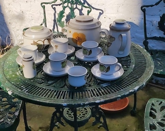 Op de afbeelding: Een groene metalen tafel met een theeservies met bloemenpatroon. De set bevat een theepot, een roomkan, een suikerpot en zes kopjes en schoteltjes.