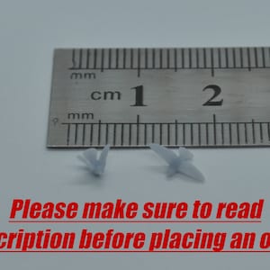 May include: Two small, light blue, plastic butterflies are shown next to a ruler. The ruler is marked in centimetres and millimetres. The butterflies are approximately 1 centimetre in length.