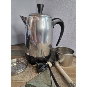 May include: A Farberware Superfast stainless steel coffee percolator with a black base and handle. Includes a filter basket, coffee scoop, and a separate stainless steel carafe. The percolator has a black power cord.