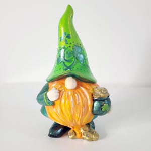 May include: A whimsical gnome figurine with a bright green hat adorned with shamrocks. The gnome has a long, orange beard and is holding a small green bag with a shamrock design. The figurine is painted with vibrant colors and has a cheerful expression.