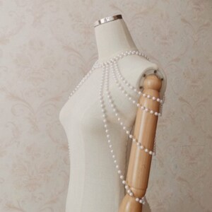 Puede incluir: Una pieza de joyer&iacute;a de cuerpo de cadena de perlas blancas con m&uacute;ltiples hileras de perlas. La joyer&iacute;a se muestra en un maniqu&iacute; blanco.