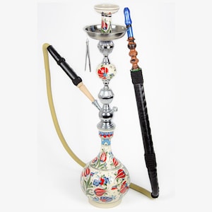 Puede incluir: Narguile decorativo con diseño floral. La base tiene forma bulbosa con flores rojas, azules y blancas. Tiene un tallo de metal plateado y una manguera negra. La cachimba está diseñada para fumar tabaco aromatizado.