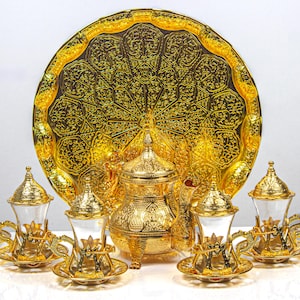 May include: A gold-colored tea set with intricate detailing. The set includes a large, round tray, a teapot, and several teacups with saucers. The design features ornate patterns and a shiny finish, suggesting a luxurious aesthetic.