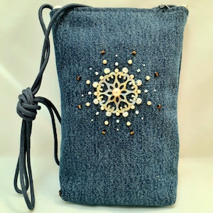 Può includere: Una piccola borsa a tracolla in denim con un decoro decorativo di perle e conchiglie al centro. La borsa ha un esterno in denim blu scuro e una tracolla regolabile nera.