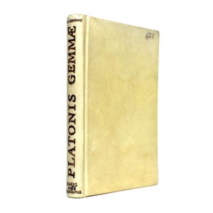 Może przedstawiać: Stara książka z kremową okładką i grzbietem. Na grzbiecie znajduje się tytuł "PLATONIS GEMMÆ" w pionowym, ciemnym tekście. Okładka książki jest lekko postarzała, z odręcznym numerem w prawym górnym rogu. Książka jest na białym tle.