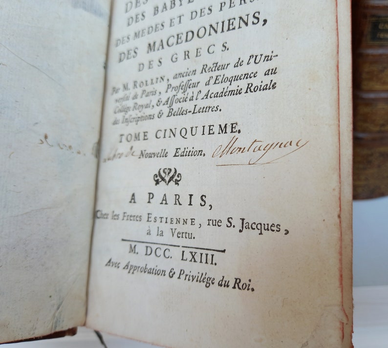 May include: Open book with text in French. The title includes "DES BABYLONIENS, DES MEDES ET DES PERSES, DES MACEDONIENS, DES GRECS." The text also includes "TOME CINQUIEME" and "A PARIS" with the date "M. DCC. LXIII."