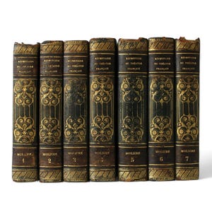 May include: A collection of seven antique books with dark covers and gold decorative accents. The spines feature gold lettering and ornate designs. The books are labeled "Répertoire du Théâtre Français" and numbered 1 through 7.