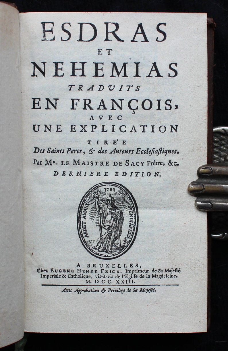 May include: A vintage book cover with the title "ESDRAS ET NEHEMIAS TRADUITS EN FRAN&Ccedil;OIS, AVEC UNE EXPLICATION TIREE Des Saints Peres, & des Auteurs Eccleſiaſtiques. Par MR. LE MAISTRE DE SACY Pr&ecirc;tre, &c. DERNIERE EDITION." The book was published in Brussels by Eugene Henry Frick in 1723.