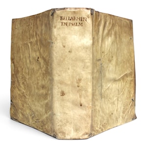 May include: An antique book with a weathered, light tan vellum cover. The spine features the hand-lettered text "BELLARMIN IN PSALM" in dark ink. The cover material shows natural creases, organic texture, and subtle discoloration throughout the surface.