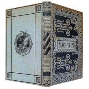 May include: A vintage book cover with a blue and white background. The title "Comedias Escogidas" is printed in black lettering. The author's name "Moratin" is printed in white lettering on a black background. The book cover features an ornate design with gold accents.