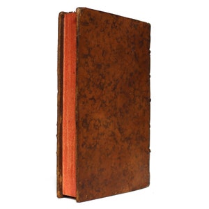 May include: A brown leather-bound book with a red spine. The book is closed and the spine is visible.