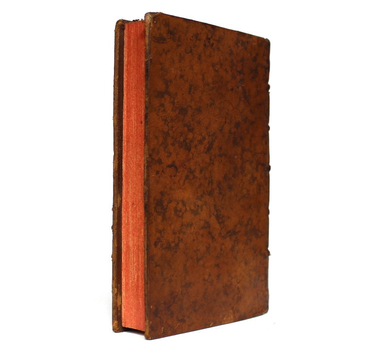 May include: A brown leather-bound book with a red spine. The book is closed and the spine is visible.