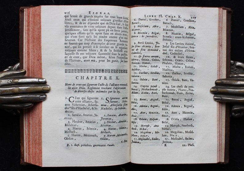 May include: An open book with yellowed pages and a brown leather cover. The book is titled "Esdras" and the text is in French. The book is open to Chapter 10 and includes a list of names.