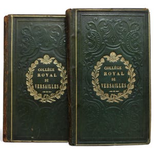 May include: Two antique books with dark green covers. The covers feature embossed floral designs and gold lettering that reads "COLLEGE ROYAL DE VERSAILLES" within a wreath. The edges of the books are worn, showing their age.