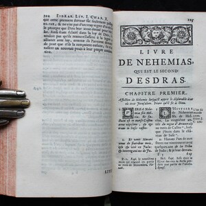 May include: A vintage book with a worn leather cover and a title page for the book of Nehemiah. The title page is in French and reads "Livre de Nehemias, Qui est le second desdras".