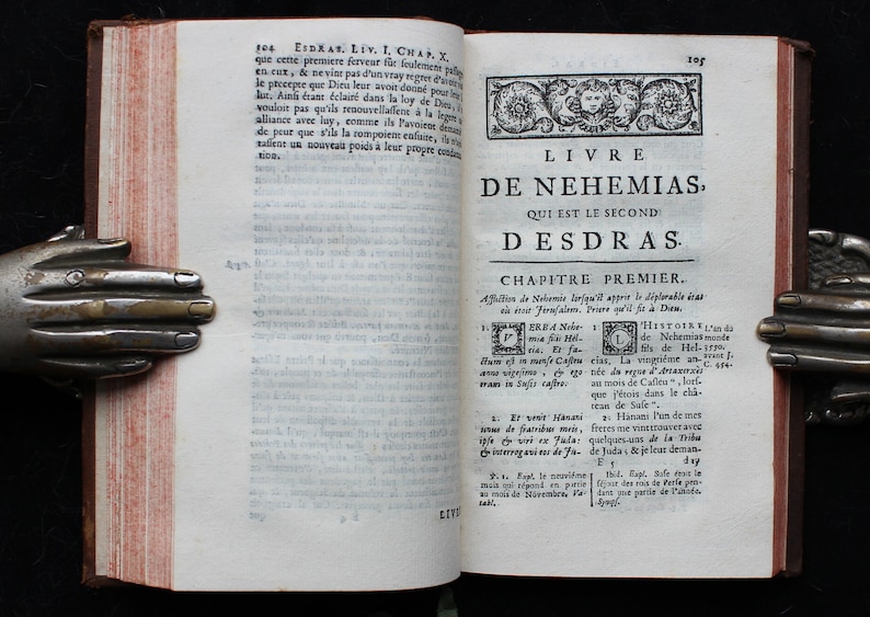 May include: A vintage book with a worn leather cover and a title page for the book of Nehemiah. The title page is in French and reads "Livre de Nehemias, Qui est le second desdras".