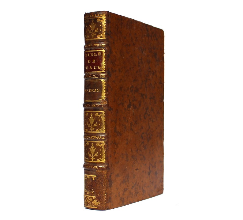 May include: A brown leather-bound book with gold accents and the text "Bible de Sacy" on the spine.