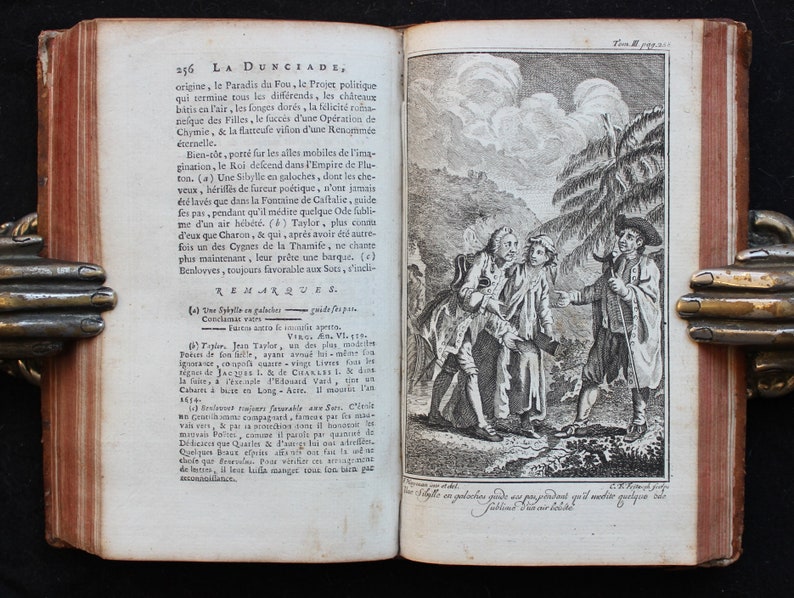 May include: A black and white illustration of three men in a forest setting. The men are dressed in long coats and hats. The man on the right is holding a staff. The illustration is from a book titled "La Dunciade".