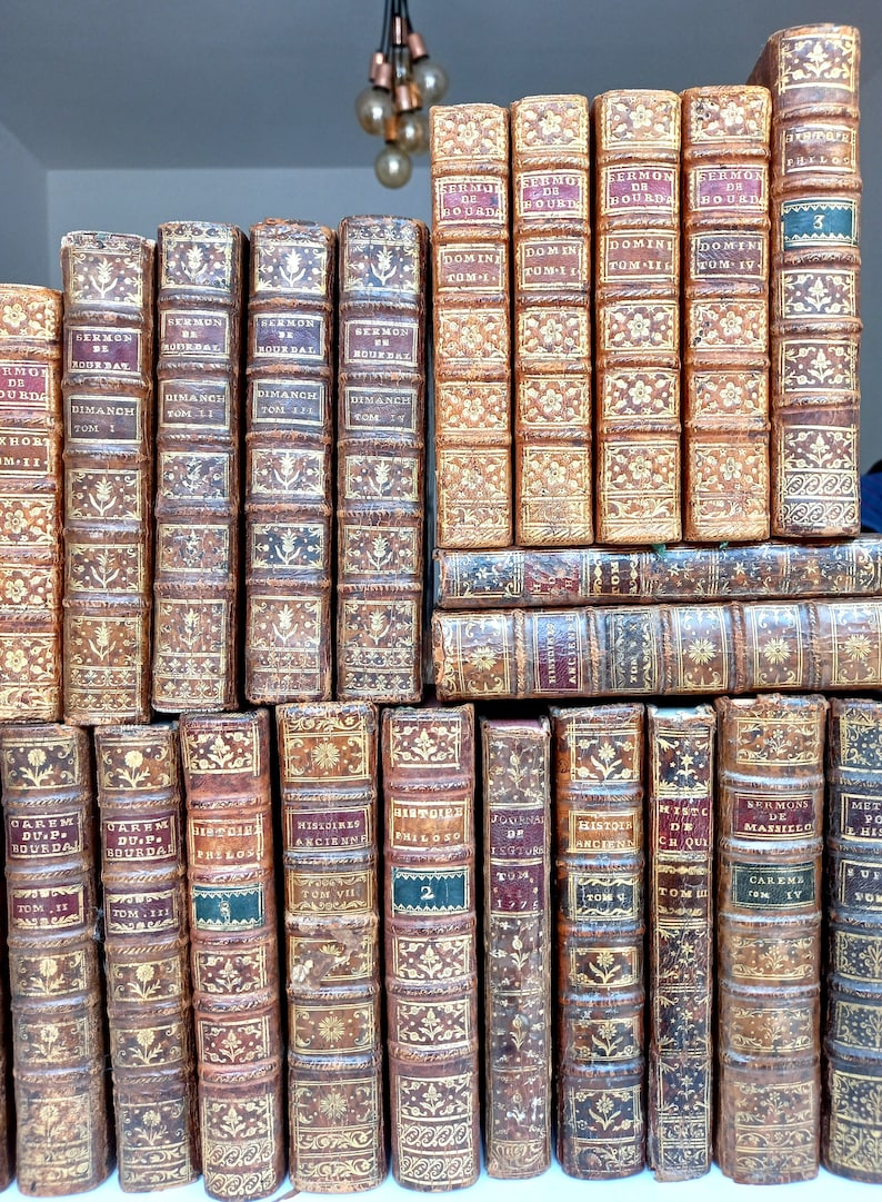 May include: A collection of antique books with leather-bound covers. The spines display titles in gold lettering and decorative patterns. The books are arranged in neat rows, showcasing their aged appearance and historical significance.