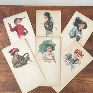 May include: A collection of vintage postcards featuring illustrations of women in various activities and attire. The cards showcase women with hats, holding an umbrella, and driving a car. The color palette includes red, blue, and brown tones.