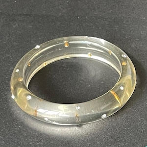 以下が含まれることがあります： ゴールドとシルバーのアクセントが付いた透明なバングルブレスレット。透明なブレスレットは丸みを帯びたデザインです。ゴールドとシルバーのアクセントはブレスレットの周りに均等に配置され、輝きとエレガンスを添えています。