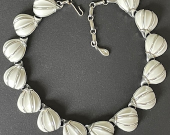 Puede incluir: Un collar blanco y plateado con una cadena y una serie de colgantes en forma de lágrima. Cada colgante tiene un diseño acanalado en relieve.