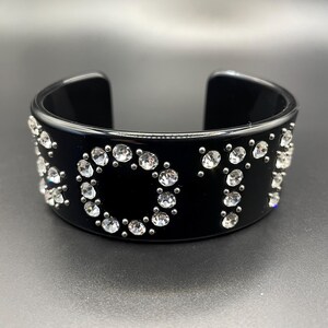 May include: Black plastic bangle bracelet with the word "VOTE" spelled out in rhinestones.
