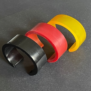 May include: Three stackable bangle bracelets in black, red and yellow. The bracelets are made of a smooth, glossy material.