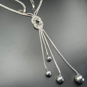 Puede incluir: Un collar de plata con un diseño anudado y cuatro bolas colgantes al final.