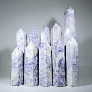 May include: A group of eleven purple and white amethyst crystal points arranged in a staggered formation. The crystals are polished and have a smooth, glassy finish.
