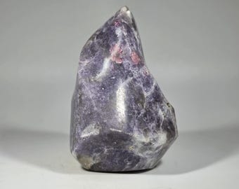 May include: A polished, flame-shaped lepidolite crystal specimen featuring a deep purple and lavender color palette with distinct, vibrant pink inclusions and a smooth, reflective surface that highlights the natural mineral texture.