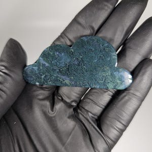 May include: A green and black agate gua sha tool shaped like a cloud. The tool is made of natural stone and has a smooth, polished surface.