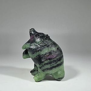 May include: A small, hand-carved bear figurine crafted from a mineral stone featuring a mottled texture. The bear is depicted in a standing, upright position with a glossy finish, showcasing vibrant shades of green, black, and hints of deep purple.