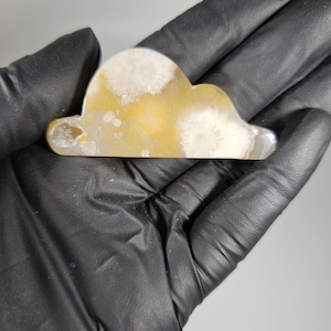 May include: A cloud-shaped decorative item with a polished surface. The item features a mix of yellow, white, and translucent colors. The cloud is held in a black gloved hand.