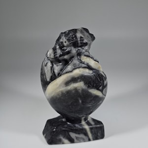 May include: A carved stone sculpture of a bear in a seated position. The sculpture is made of black and white marble, with a polished finish. The bear is sitting on a square base. The sculpture is a decorative item.