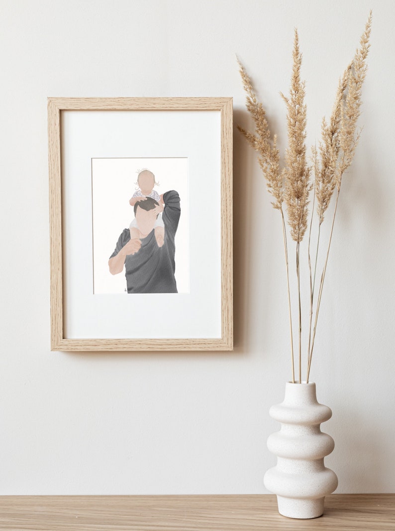 K&ouml;nnte beinhalten: Eine gerahmte Illustration von einem Vater und einem Kind. Der Vater tr&auml;gt ein dunkelgraues Hemd und das Kind tr&auml;gt ein wei&szlig;es und rosa Hemd. Die Illustration ist in einem hellen Holzrahmen.
