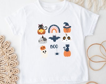 May include: White t-shirt with a variety of Halloween-themed illustrations, including a cat, a bat, a ghost, a pumpkin, and a rainbow. The text "BOO" is also included on the shirt.