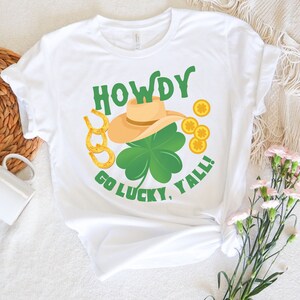 May include: White t-shirt with a green shamrock, gold horseshoes, and a cowboy hat with the text "Howdy Go Lucky, Y'all!"