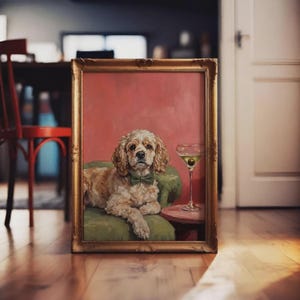 Puede incluir: Pintura enmarcada de un perro con pajarita verde, sentado en una silla verde, con una copa de martini sobre una pequeña mesa rosa. El fondo es rosa y el marco es dorado.