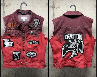 Op de afbeelding: Een mouwloos spijkergilet in een tweekleurige rode en donkerrode wassing, voorzien van metalen studs en diverse bandpatches waaronder Guns N' Roses, Thin Lizzy, Nirvana, Foo Fighters, Van Halen en een grote Led Zeppelin-rugpatch.