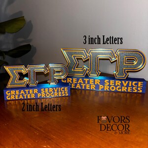 Pu&ograve; includere: Due set di lettere decorative, uno con lettere da 7,6 cm e l'altro da 5 cm. Le lettere sono dorate e nere, con le lettere greche &Sigma;&Gamma;&Rho;. Le basi blu riportano la scritta "GREATER SERVICE GREATER PROGRESS".